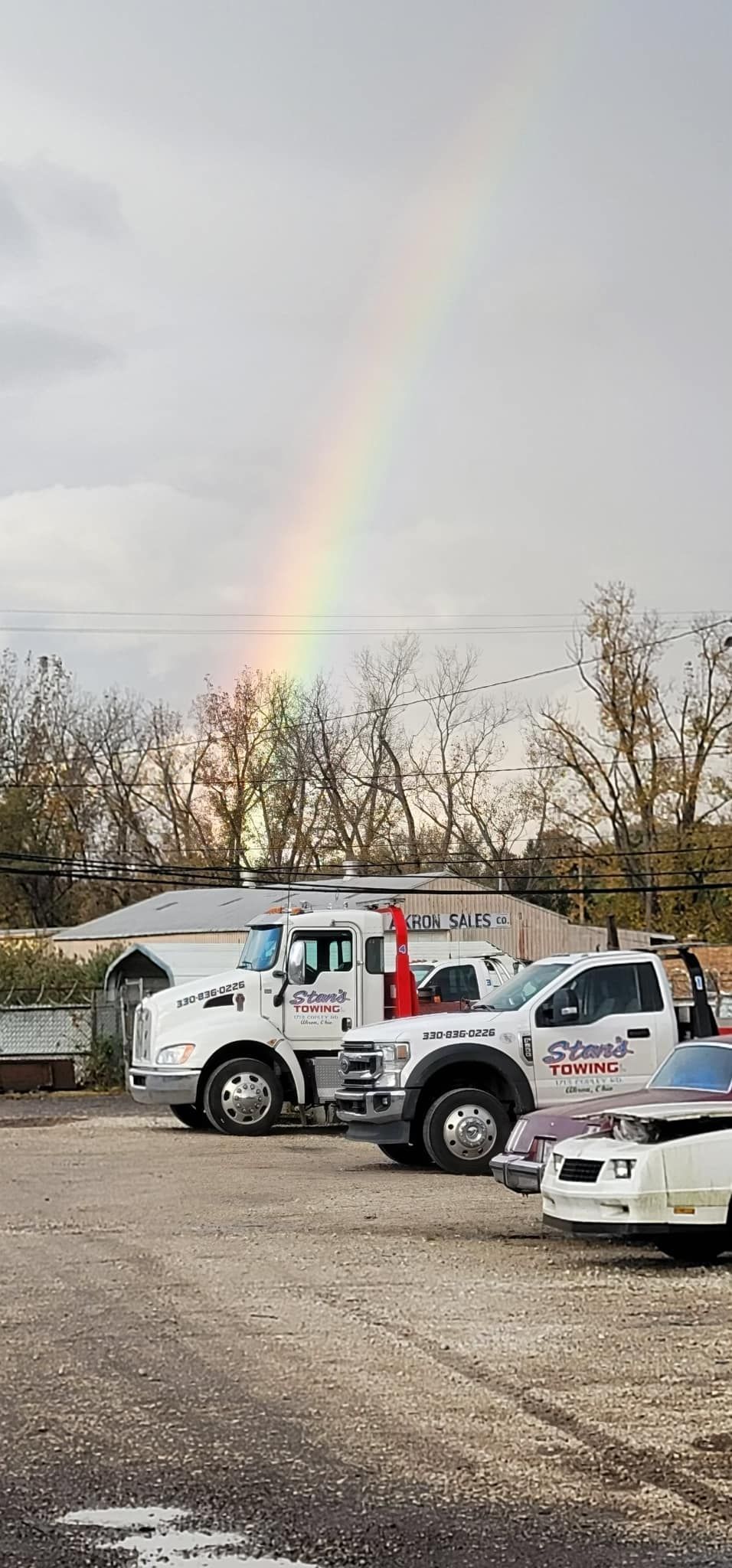 Rainbow over parked work trucks in a lot after rain