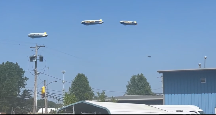 Three blimps flying over a blue industrial area on a clear day