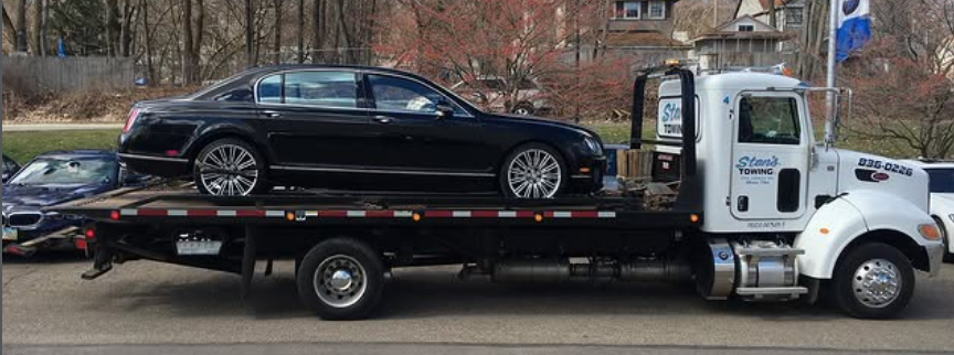 Black sedan on a flatbed tow truck on a city street