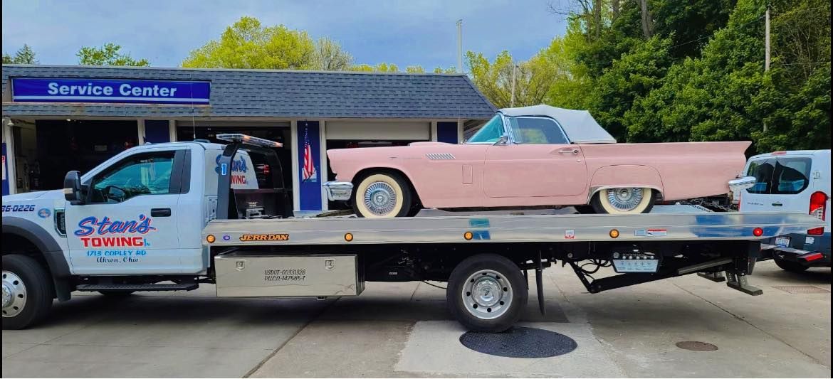 Tow truck carrying a pink classic car in front of a service center