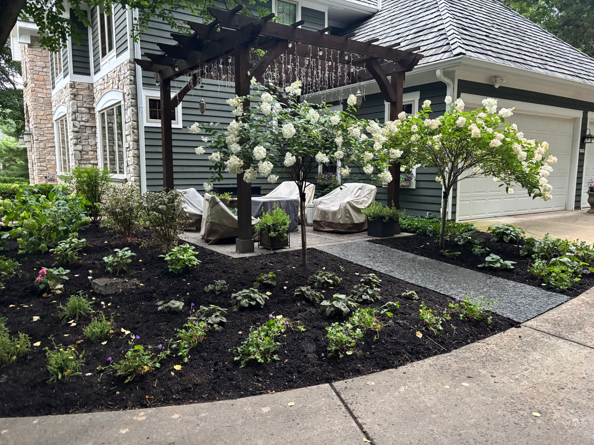 Landscaped garden with white flowering shrubs beside a stone house and covered patio