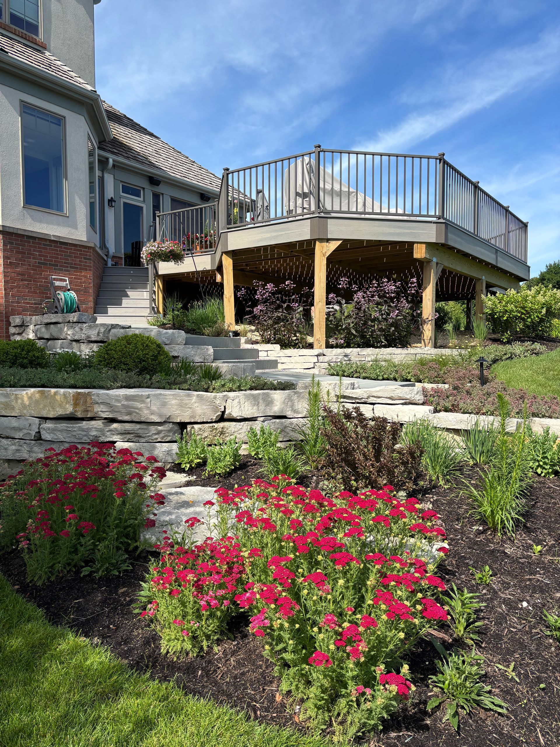 An Elevated deck above a flower bed filled with red flowered yarrow plants