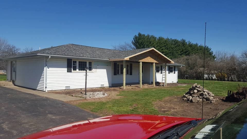A red car is parked in front of a white house.