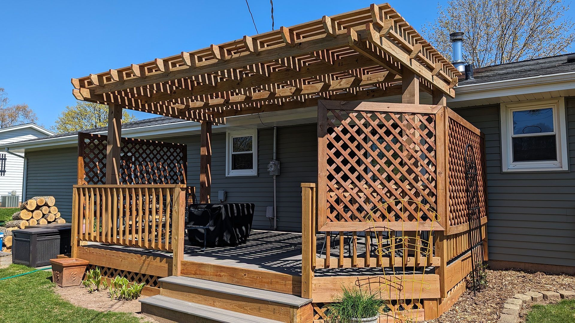 A backyard wood deck with a pergola, lattice privacy screens, and stairs, attached to a house with gray siding.