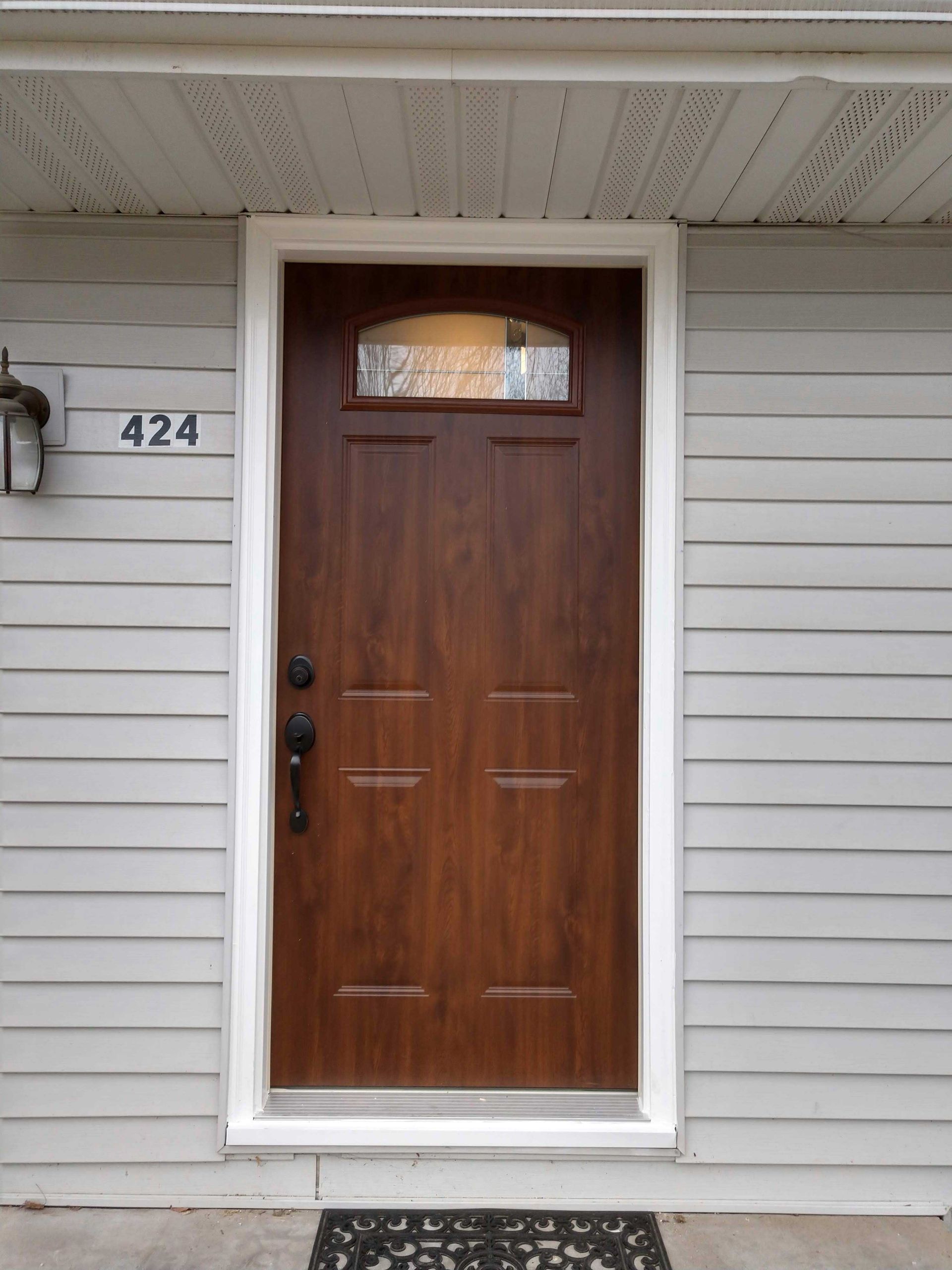Brown front door with glass transom, white trim, on gray siding. Black door handle, welcome mat, house number 424.