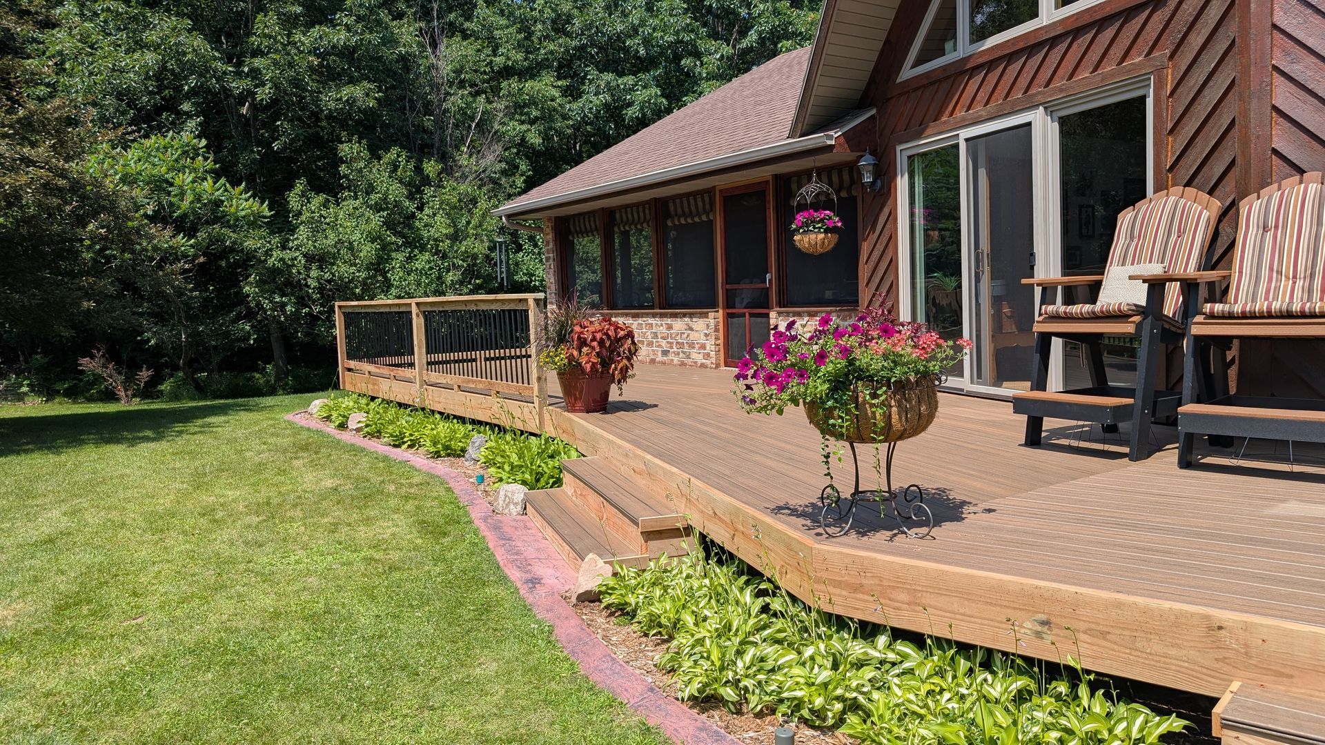 Brick house porch with wooden deck, potted flowers, and patio chairs beside a green lawn