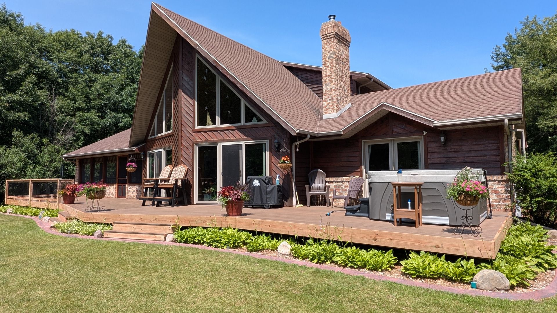 Modern A-frame house with a wood deck, large windows, chimney, and landscaped lawn under a clear sky