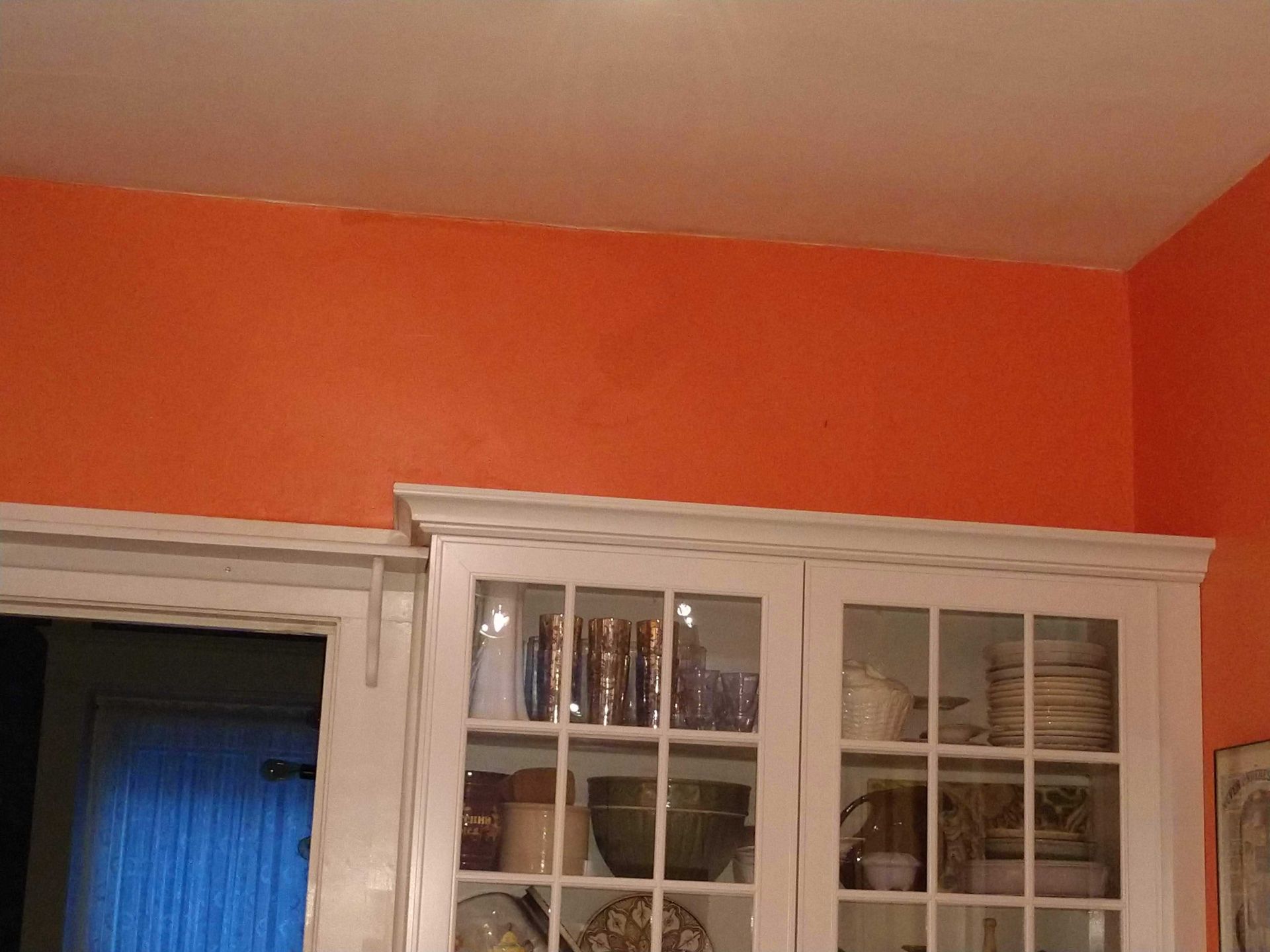 Orange wall above a white cabinet filled with dishware.