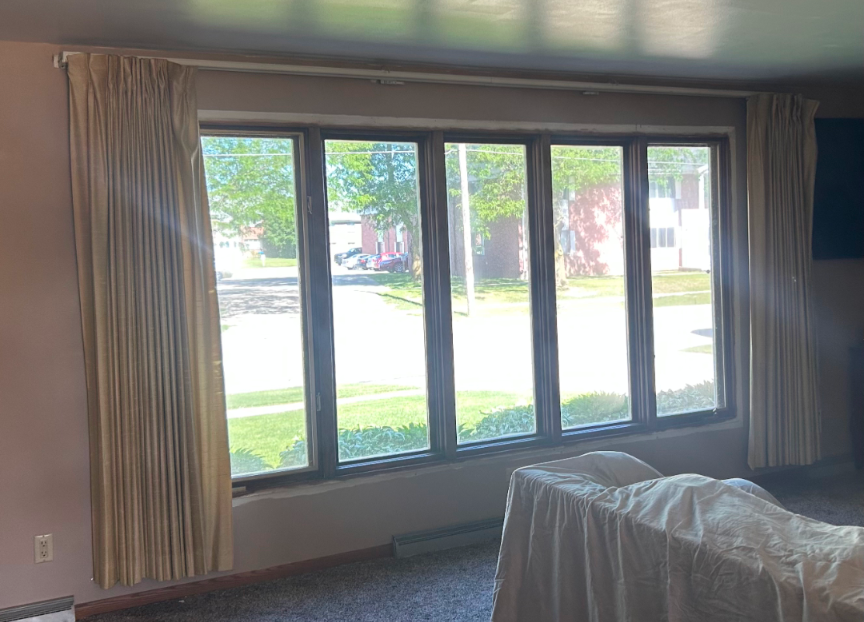 Curtained living room windows with a view of a sunlit street and green lawn outside