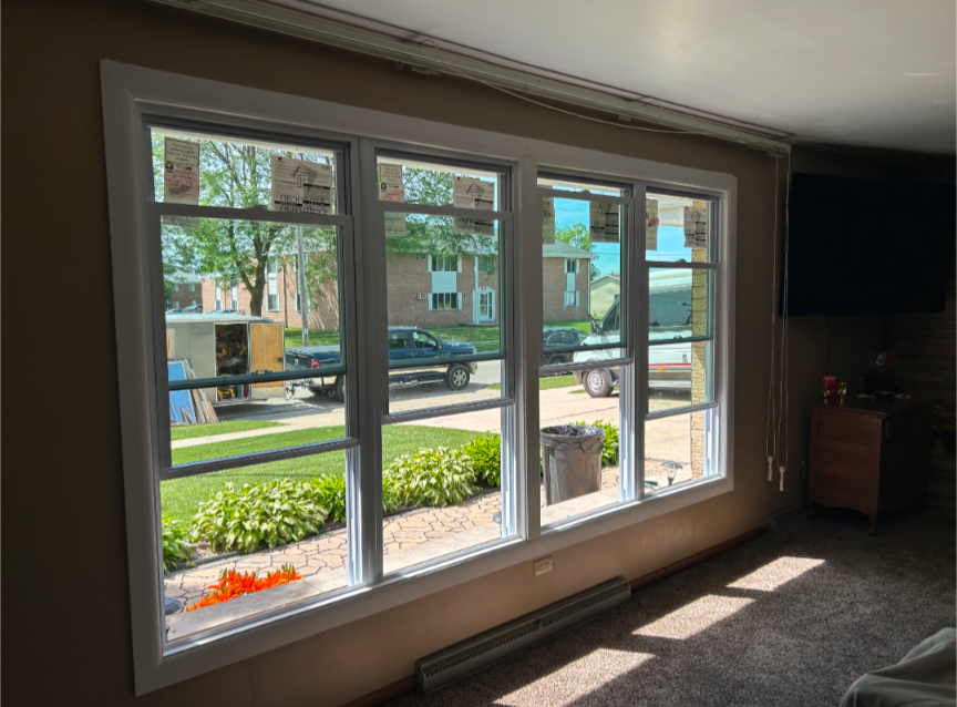 Living room bay window with sunlight, showing a street, trees, and apartment buildings outside