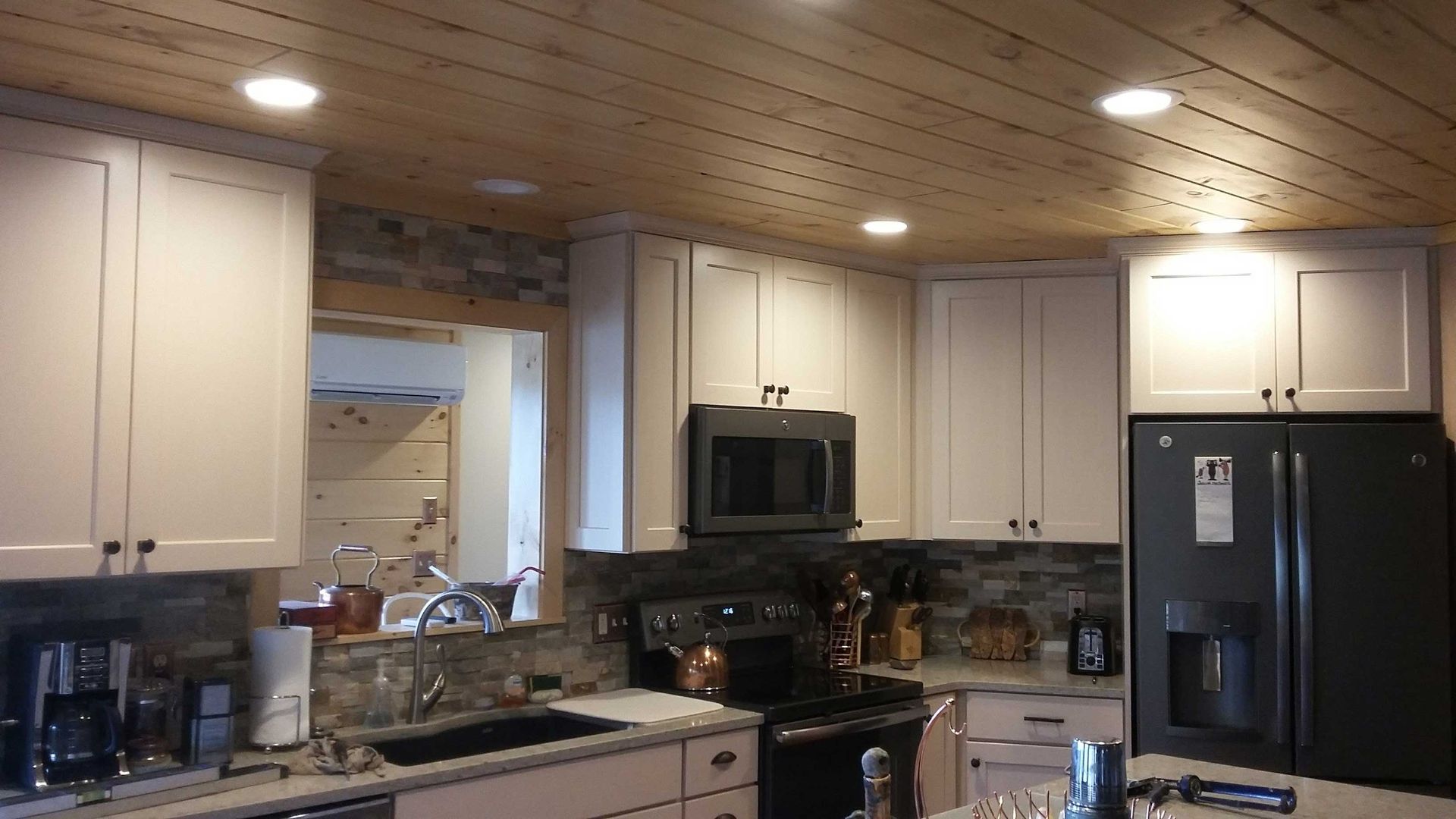 Kitchen with white cabinets, dark appliances, and a wood ceiling.
