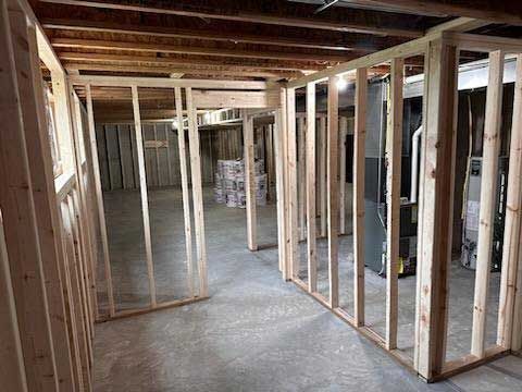Interior view of a basement under construction with wooden wall framing on a concrete floor.