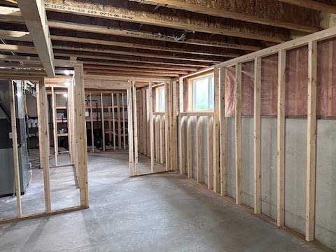 Basement interior with unfinished wooden framing for walls and ceiling, two windows, and concrete floor.