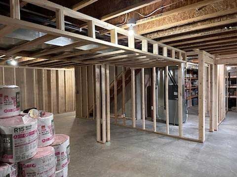 Framing of a basement with wooden studs, insulation rolls, and overhead beams.