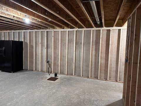Unfinished basement room with wooden wall studs, concrete floor, and black appliance.