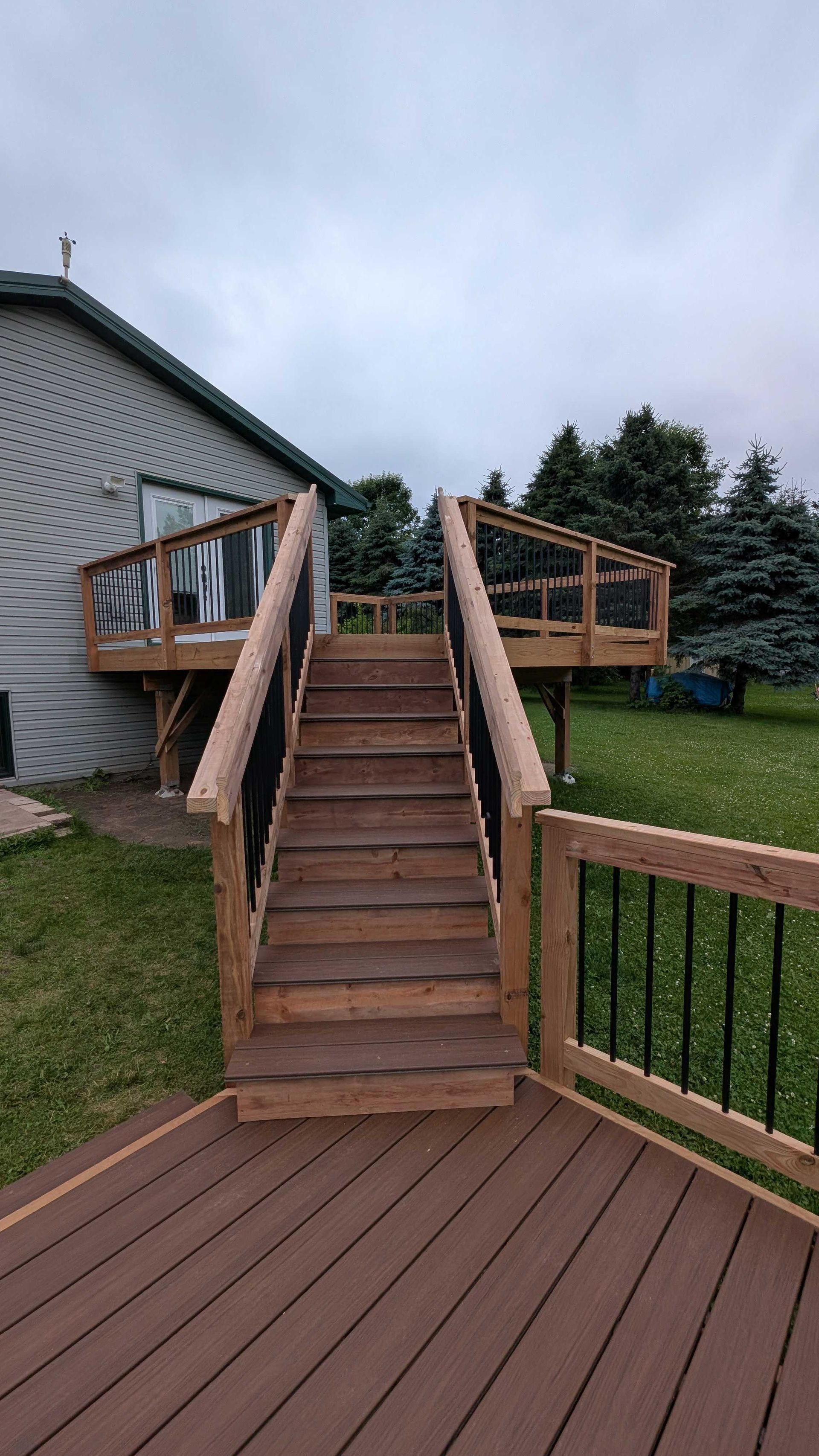 Wooden deck with stairs leading to a higher level deck attached to a house; dark gray sky in the background.