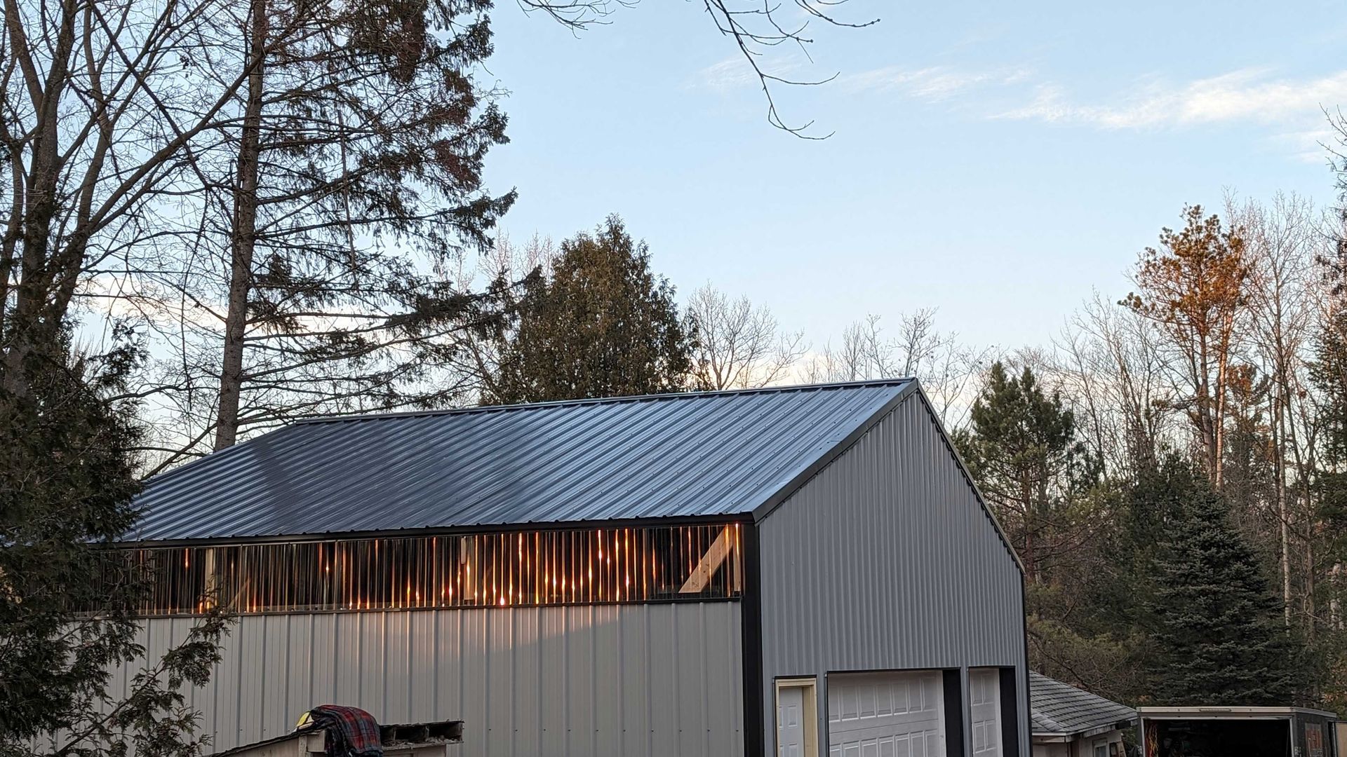Gray metal-roofed shed with missing siding, set against trees and a blue sky.