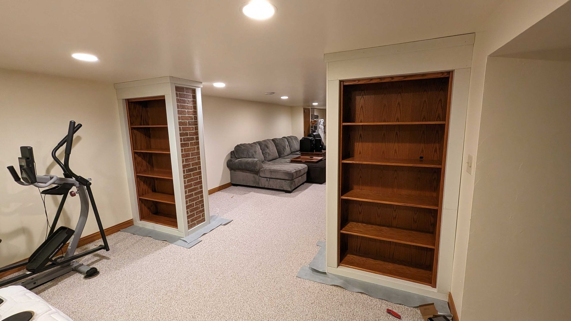 Basement room with built-in bookshelves, exercise equipment, and a couch.