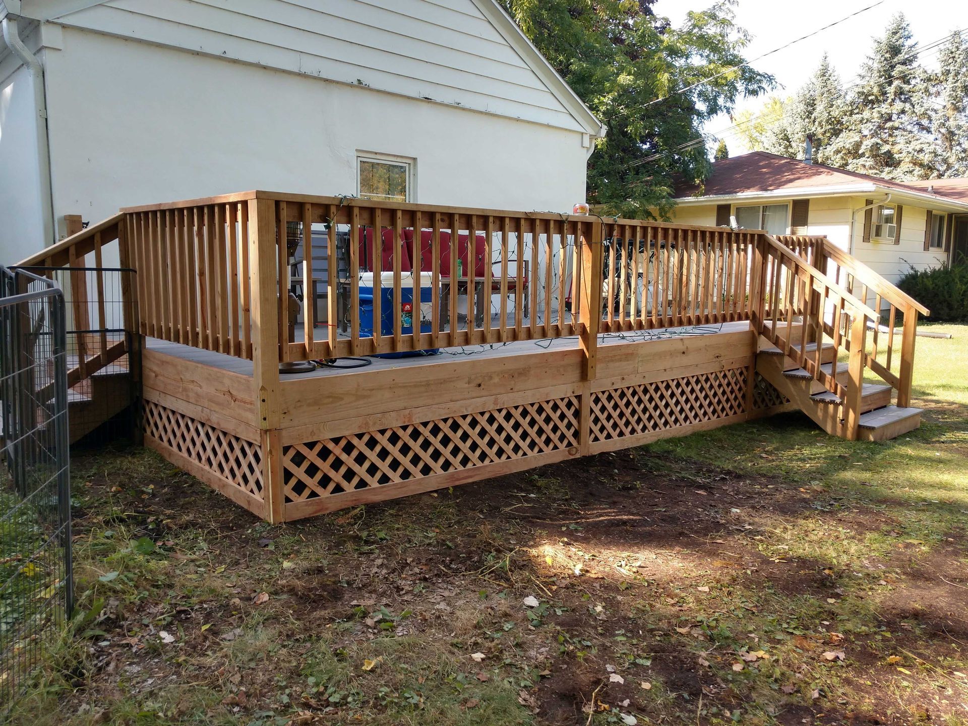 Wooden deck with latticework skirting, railings, and stairs attached to a white house.