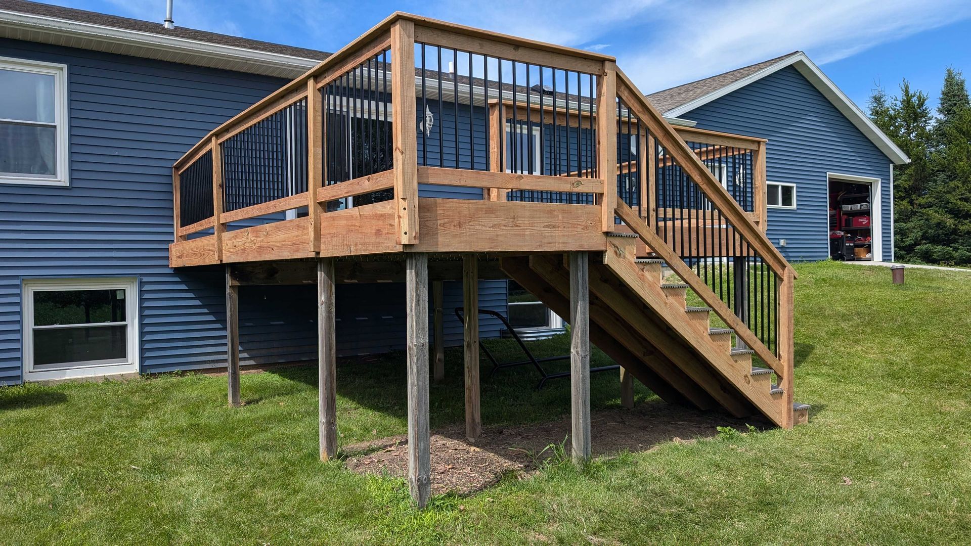 Wooden deck with stairs attached to a blue house, set on green grass.