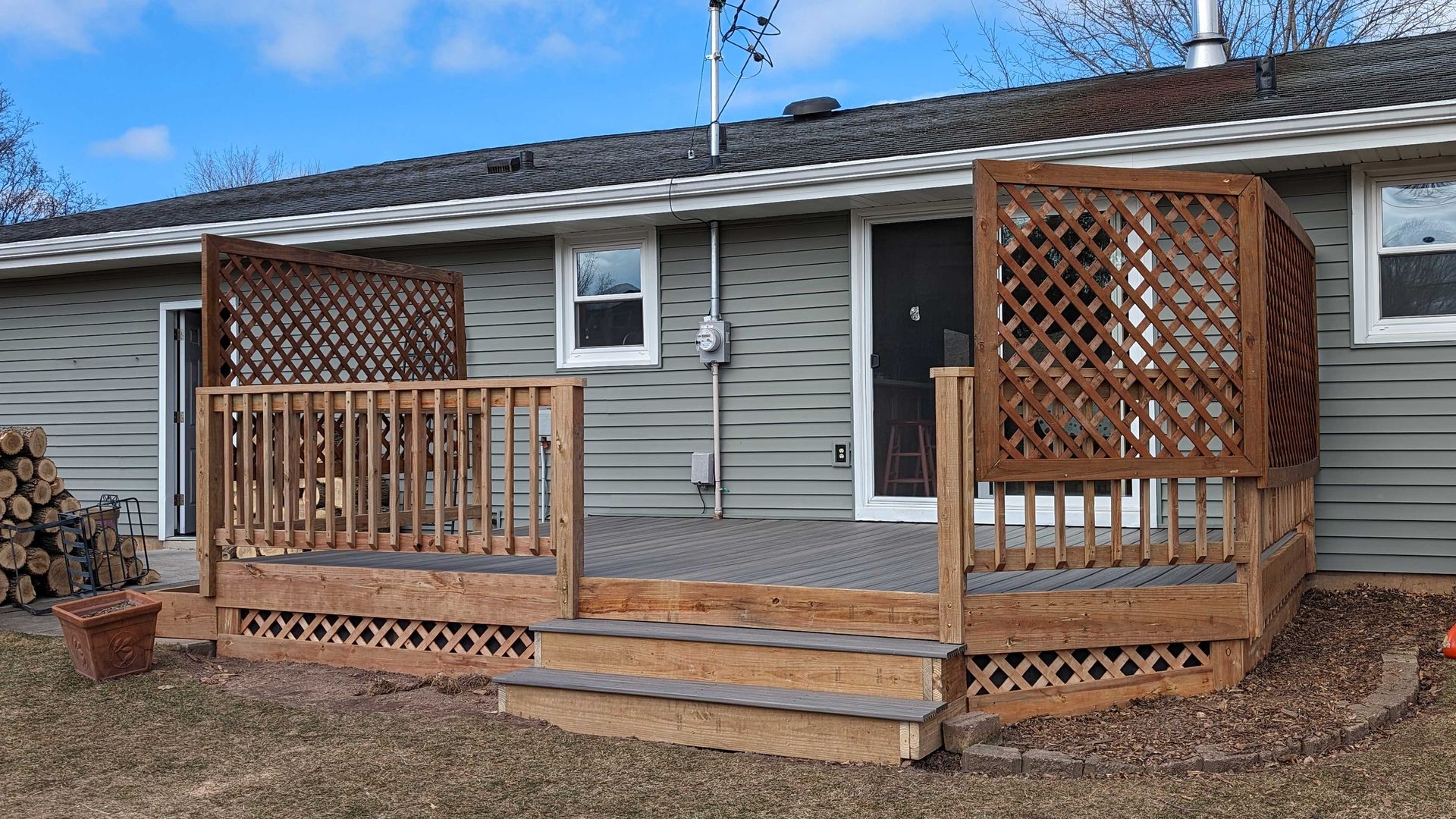 Wooden deck attached to a light green house with lattice, stairs, and a back door.