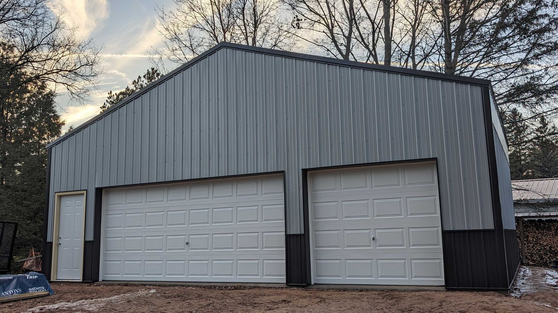 Gray metal building with two garage doors and a side door, set in a wooded area.