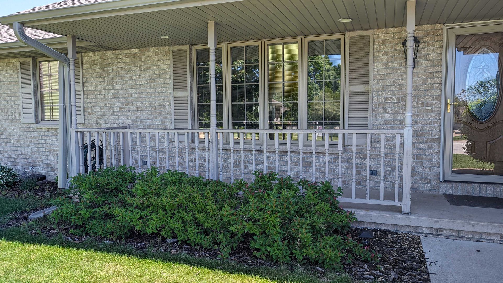 Gray stone-covered house exterior with a porch, windows, and bushes in front.