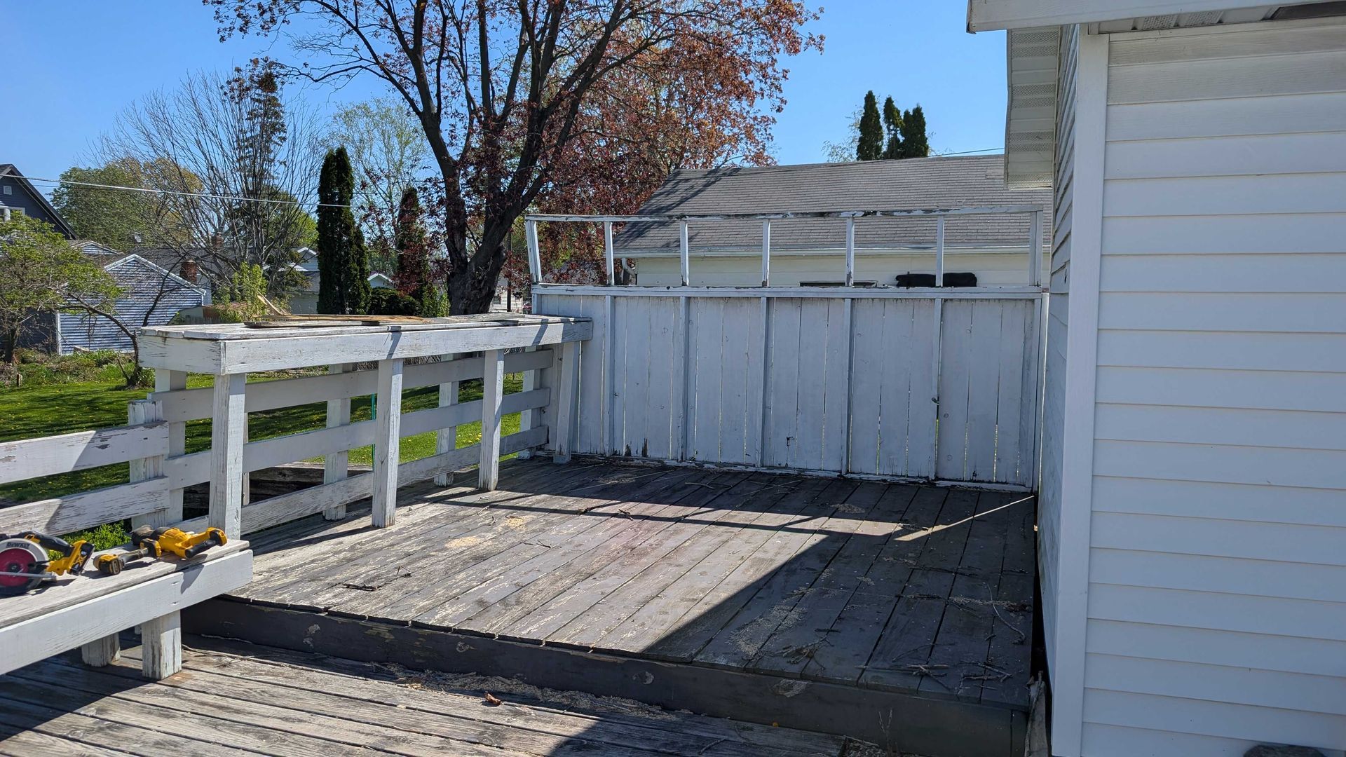 Wooden deck with weathered white railing and fence against a bright sunny sky.