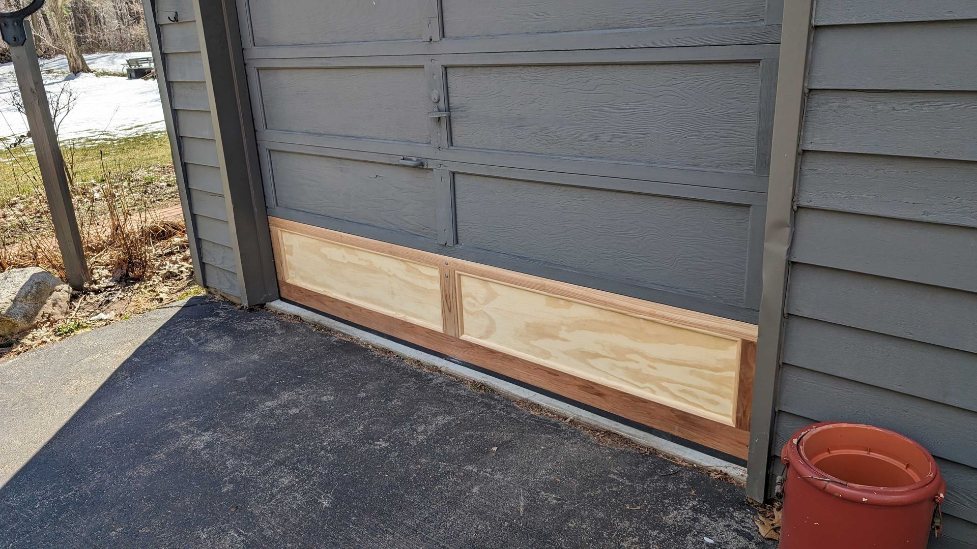 Wooden barrier installed at the base of a garage door, possibly for flood protection, asphalt driveway.