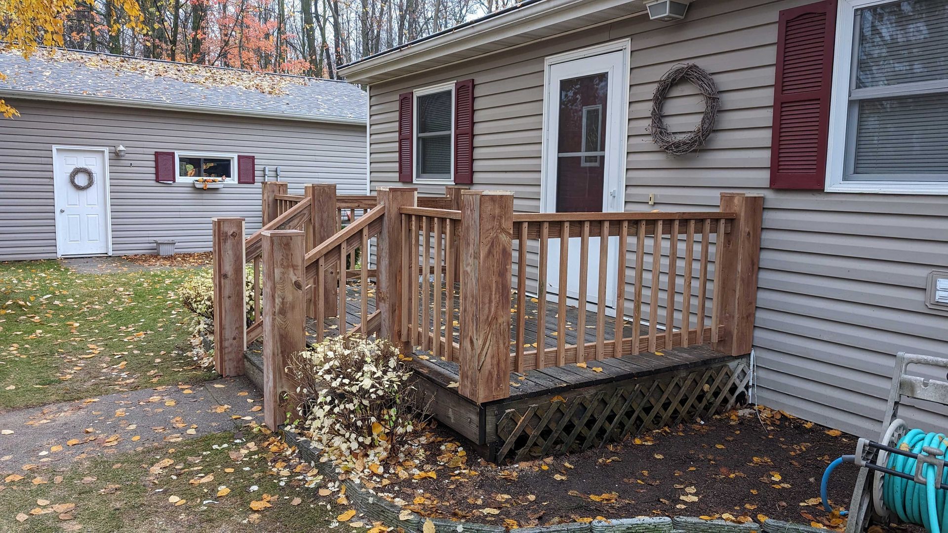 Wooden porch with railings in front of a light brown house with red shutters.