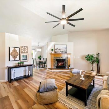 A modern living room with a stone fireplace, wood floors, a dark console table, and a large ceiling fan.