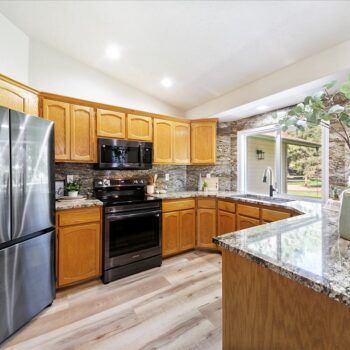 Modern kitchen with honey-oak cabinets, stainless steel appliances, granite countertops, and light wood-plank flooring.