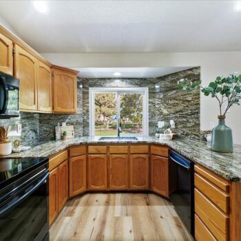 A U-shaped kitchen with honey-oak cabinets, dark granite countertops and backsplash, and a window over the sink.