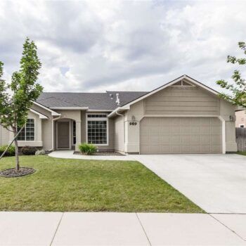 A single-story, beige suburban house with a dark gray shingled roof, a two-car garage, and a small front lawn.