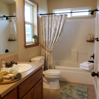 A bright bathroom with a wood vanity, white sink, toilet, and a bathtub with a beige curtain and white tiles.