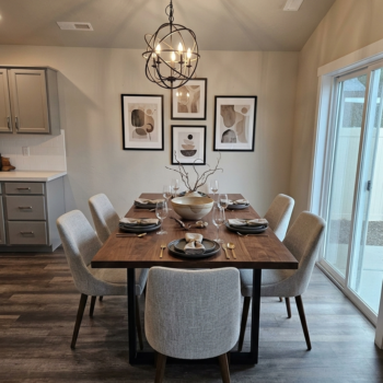 A modern dining room featuring a wooden table with six light gray chairs, a globe pendant light, and framed wall art.