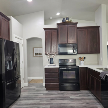 A kitchen with dark wood cabinets, black appliances, light grey walls, and grey wood-look flooring.