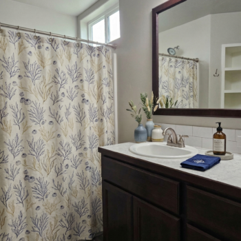 A bathroom with a dark wood vanity, a marble-topped counter, a mirror, and a cream-colored shower curtain with blue coral.
