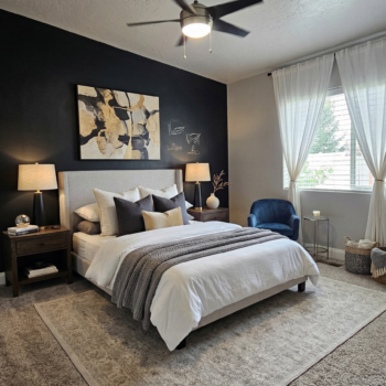 A bedroom with a black accent wall, a cream upholstered bed, white curtains, and a blue armchair on a neutral rug.