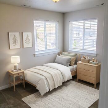 A cozy bedroom with a twin bed, wooden nightstand, light wood dresser, and two fern art prints on a beige wall.