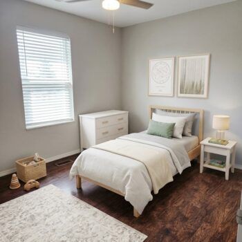 A bright, minimalist bedroom with a twin bed, a white dresser, a nightstand with a lamp, and a rug on wood flooring.