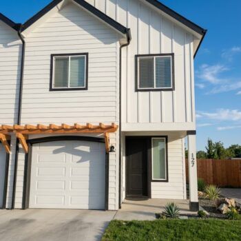A two-story white townhouse with black trim, a wooden pergola over the garage, and number 127 by the front entrance.