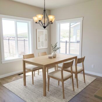 A modern, light-wood dining set with four cushioned chairs sits on a woven rug beneath a five-light chandelier.