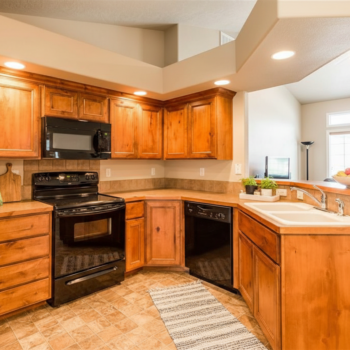 A kitchen featuring natural wood cabinets, black appliances, a double-basin sink, and a striped runner rug.