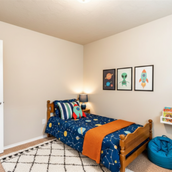 A child’s bedroom with a space-themed bed, a patterned rug, wall art depicting space, and a blue beanbag chair.