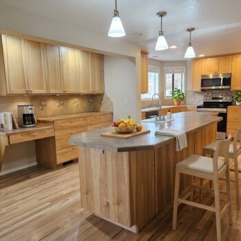A bright, modern kitchen with light wood cabinets, a spacious island, two bar stools, and hardwood floors.