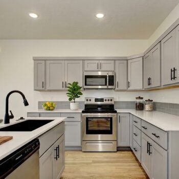 A modern U-shaped kitchen with light gray cabinets, stainless steel appliances, white countertops, and a black sink.