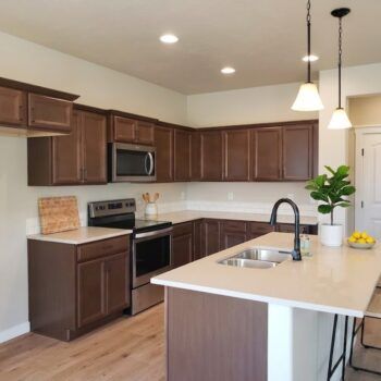 A modern kitchen with dark wood cabinets, stainless steel appliances, white countertops, and two pendant lights above.