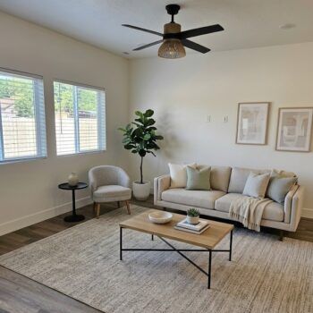 A neutral-toned living room featuring a beige sofa, a light wood coffee table, an armchair, and a potted faux plant.
