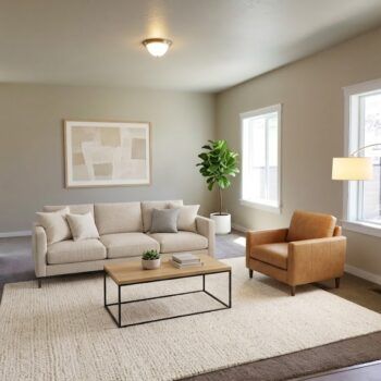 A modern living room with a beige sofa, leather armchair, coffee table, potted plant, wall art, and a beige area rug.